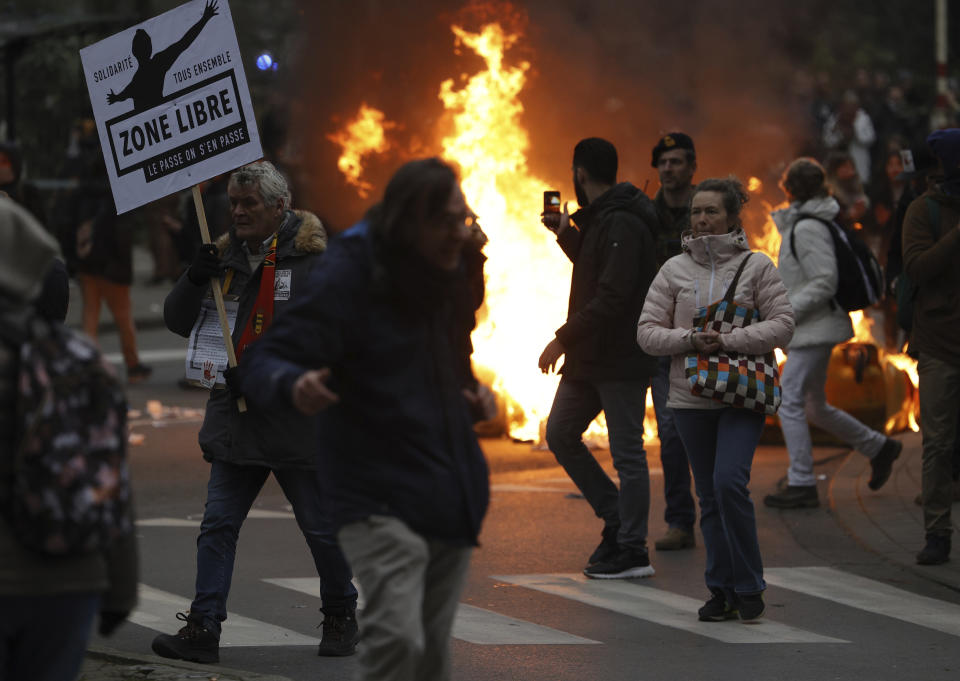 Protestors wave signs near a burning fire as they demonstrate against COVID-19 measures in Brussels, Sunday, Jan. 23, 2022. Demonstrators gathered in the Belgian capital to protest what they regard as overly extreme measures by the government to fight the COVID-19 pandemic, including a vaccine pass regulating access to certain places and activities and possible compulsory vaccines.(AP Photo/Olivier Matthys)