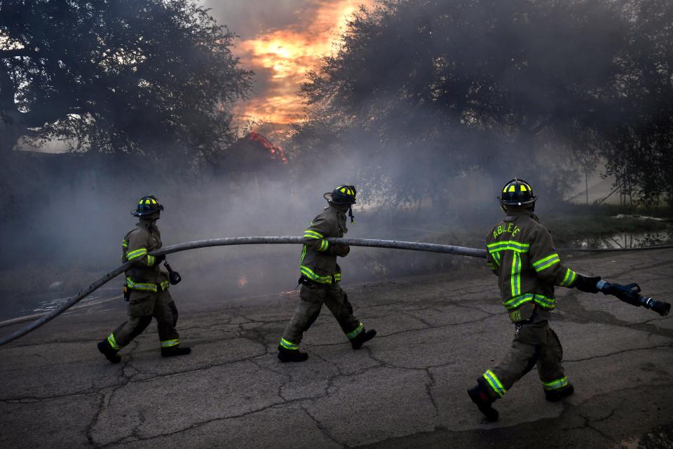 Abilene firefighters carry a hose down Cypress Street as they knock down a morning blaze at the abandoned St. Ann's Hospital on Tuesday.