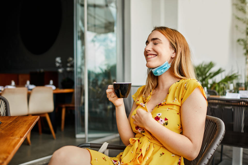 Woman sipping coffee at a restaurant with mask under her face