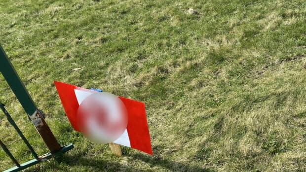 An altered paper sign that resembled a Canadian flag with the maple leaf replaced by a swastika symbol was found on the front lawn of CBC Windsor.  (CBC News - image credit)