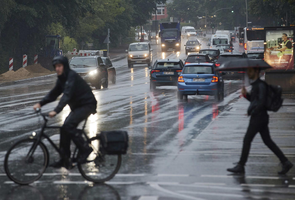 A cyclist and a passer-by with an umbrella cross a traffic light intersection during rainfall in Hamburg, Germany, Monday, June 21, 2021. (Georg Wendt/dpa via AP)