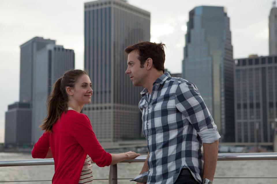 in a scene, Alison and Jason conversing by a railing with city skyline behind, from the movie "Sleeping with Other People"