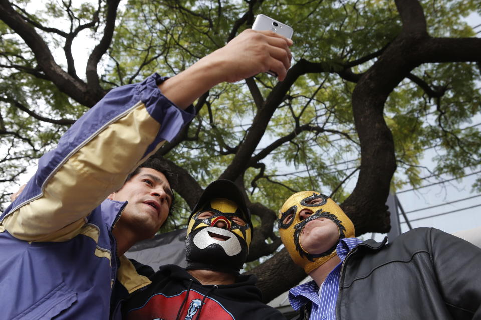 Fans take a selfie with Mexican wrestlers Super Muñeco, center, and Sanguinario, right, before "lucha libre" match in Mexico City, Saturday, Dec. 21, 2019. Mexican wrestling, otherwise known as the “lucha libre,” is a highly traditional form of light entertainment masquerading as a ‘sport’. (AP Photo/Ginnette Riquelme)