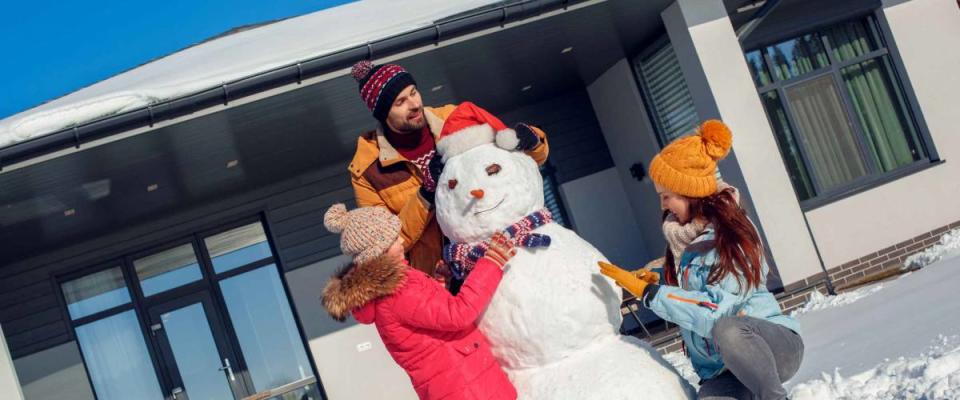 Family on a winter vacation spending time together outdoors standing near the house making snowman smiling concentrated