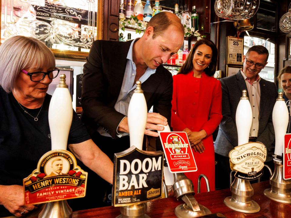 Prince William, Prince of Wales (2nd L) flanked by Britain's Catherine, Princess of Wales (C), serves a beer during a visit of the Dog & Duck Pub in Soho, central London, on May 4, 2023