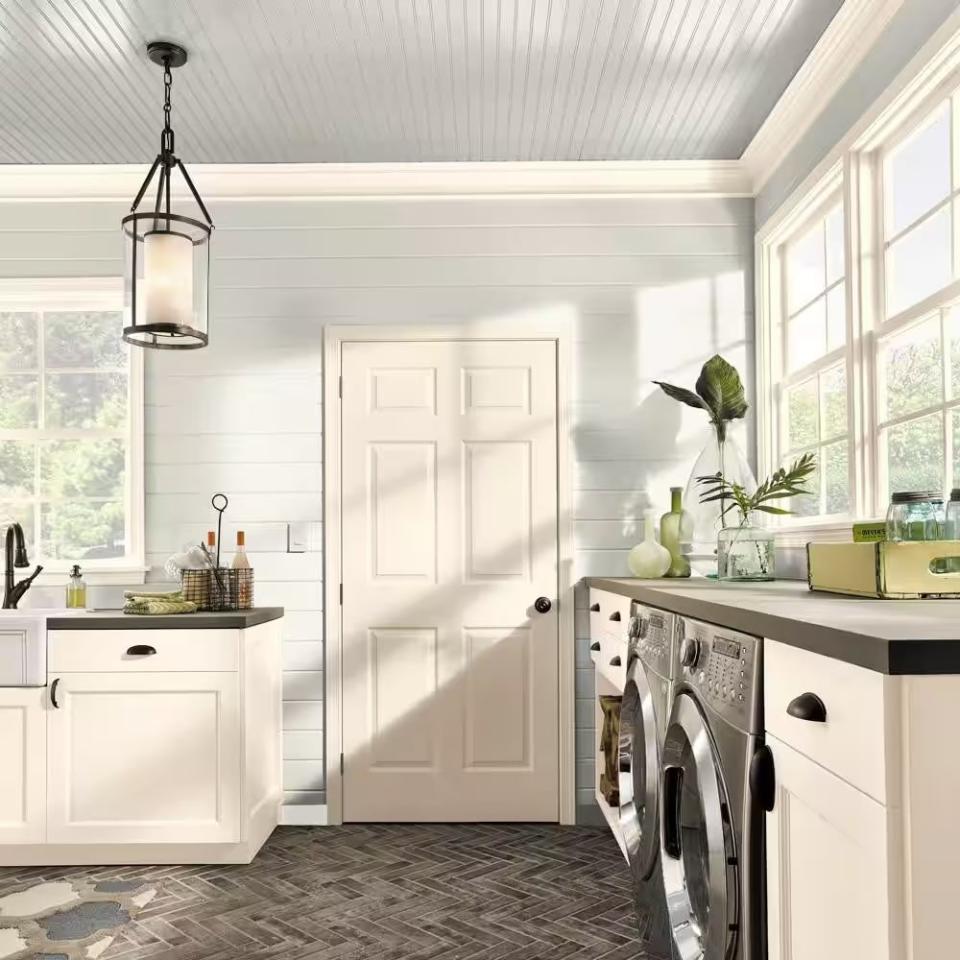 A hyper-realistic 3D render of a bright, modern laundry room with cabinets and a door painted in Swiss Coffee by Behr. 