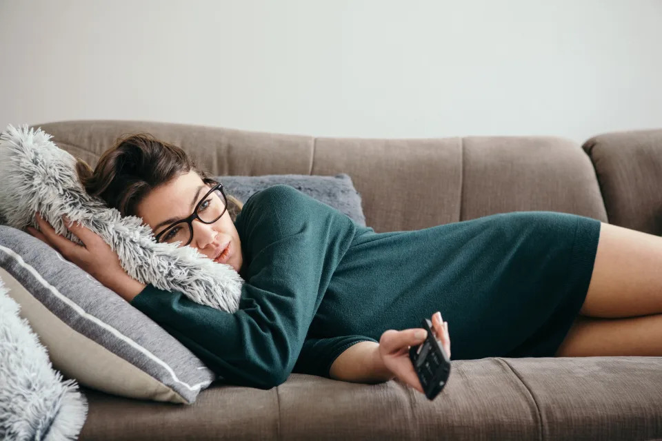 Woman lounging on sofa with remote, appearing relaxed and comfortable