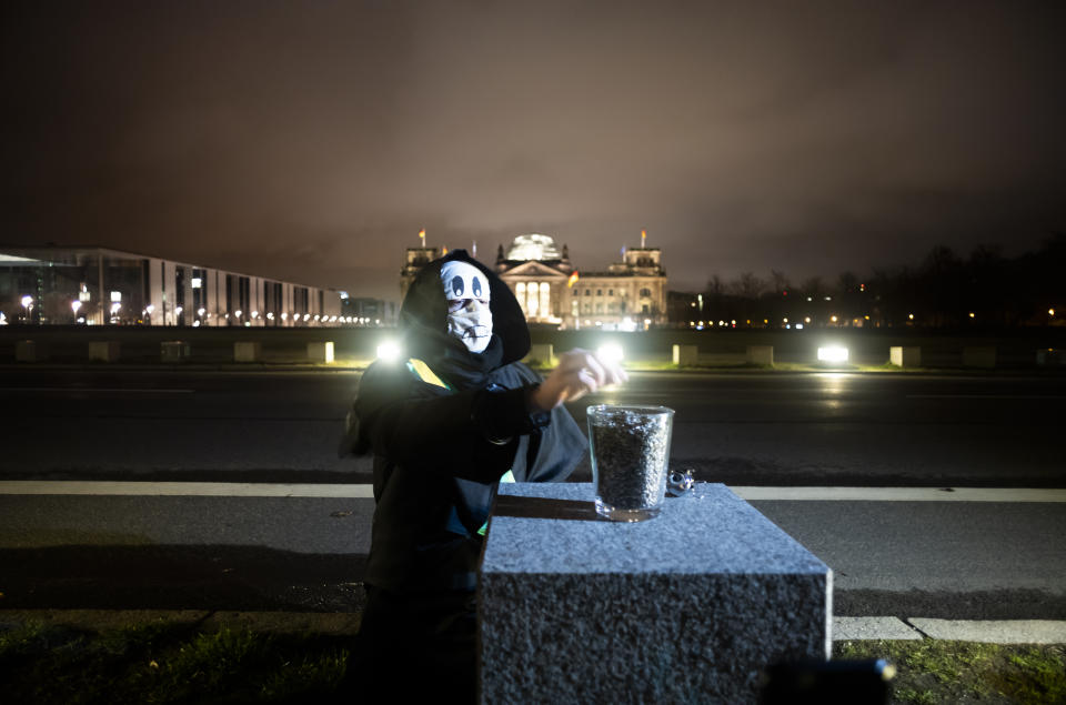Brazilian activist and artist Rafael Puetter, dressed as the grim reaper, sits in front of the Reichstag building and counts sunflower seeds during a one-man protest through Berlin, Germany, early Wednesday, April 7, 2021. The multimedia artist starts his performance at the Brazilian embassy in Berlin at midnight every night to protest against Brazil's COVID-19 policies. Rafael Puetter walks to the Brandenburg Gate and then to the nearby German parliament building, in front of which he counts out a sunflower seed to represent each of the lives that were lost over the past 24 hours in Brazil because of the coronavirus pandemic. (AP Photo/Markus Schreiber)