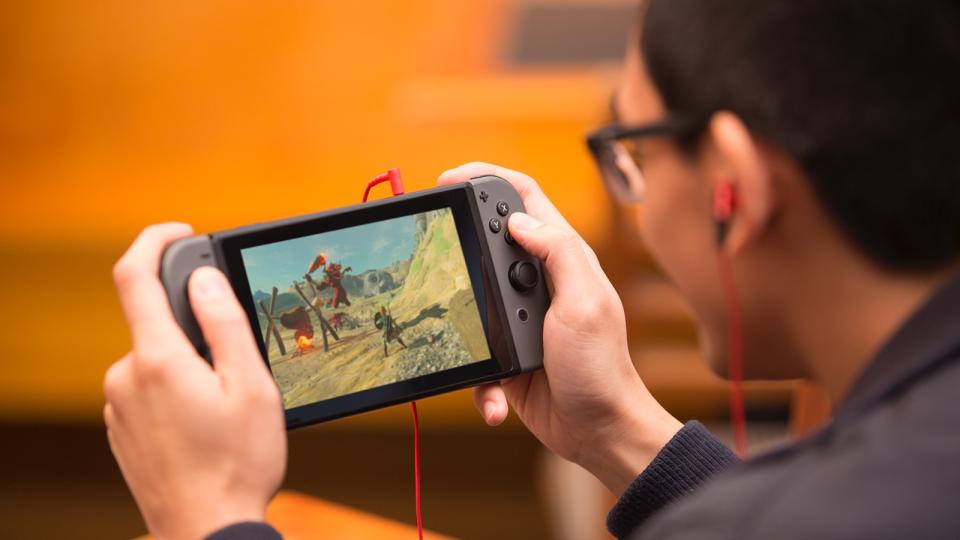 Man playing game on a Nintendo Switch with red ear buds plugged in