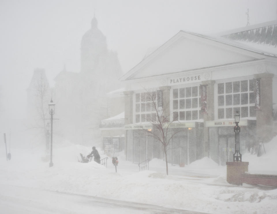 A man clearing snow off the the sidewalk in front of the Fredericton Playhouse, New Brunswick, Canada./Getty Images