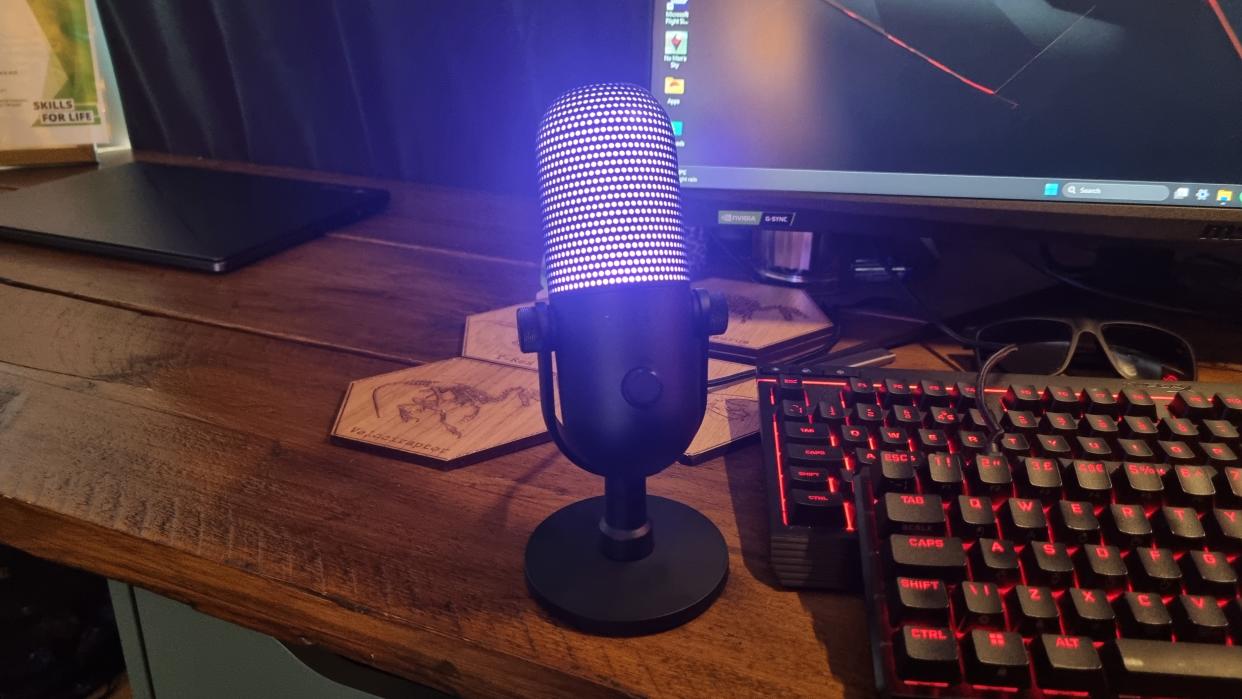  The Razer Seiren V3 Chroma desktop microphone, standing on a desk and lit up in pink. 