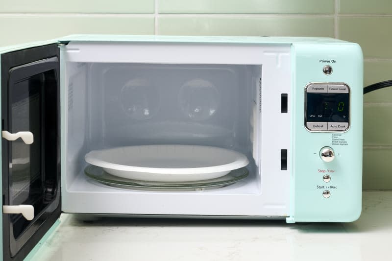 head on shot of a paper plate sitting in a light blue microwave with the door open.