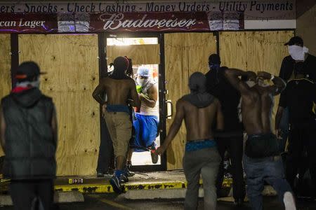 A masked man carries items out of a liquor store that had been broken into during on-going demonstrations to protest against the shooting of Michael Brown, in Ferguson, Missouri, August 16, 2014. REUTERS/Lucas Jackson