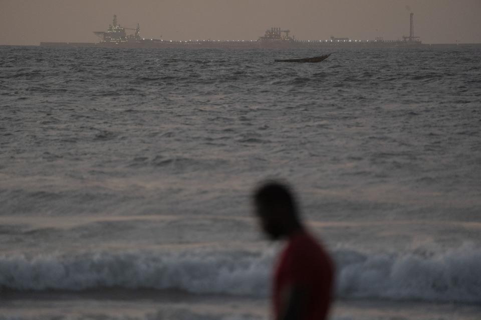 A man walks on the beach past an offshore gas terminal in Saint Louis, Senegal, Thursday, Jan. 19, 2023. The rig was the final straw for Saint-Louis, pushing it to the brink of economic disaster, according to locals, officials and advocates. (AP Photo/Leo Correa)