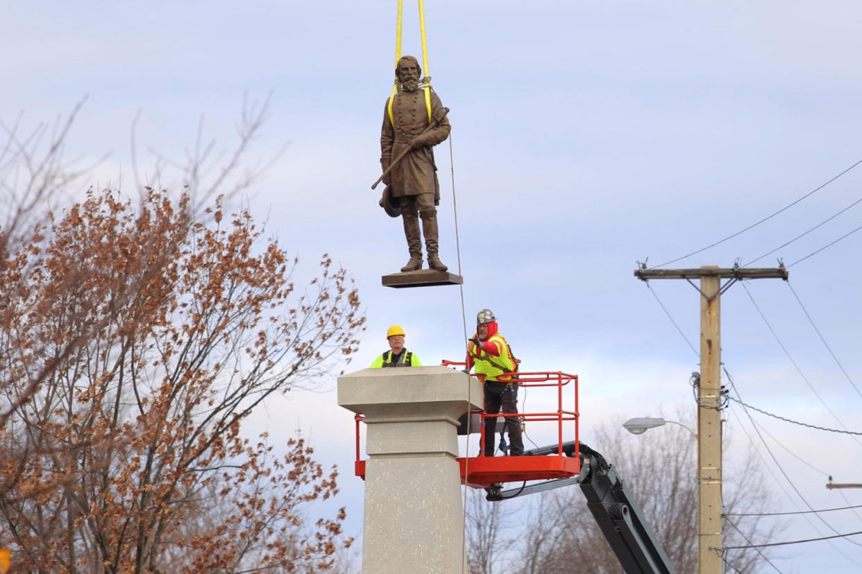 A statue of Confederate General Ambrose P. Hill is lifted off its pedestal as two workers look on.