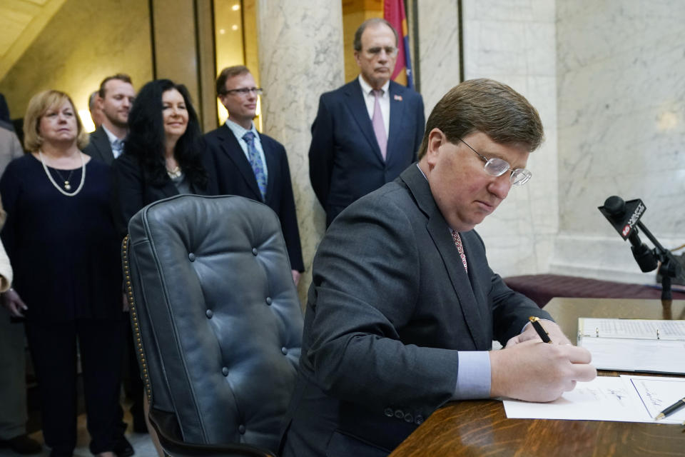 Mississippi Gov. Tate Reeves signs the first state bill in the U.S. this year to ban transgender athletes from competing on female sports teams, as supporting lawmakers gather behind him, Thursday, March 11, 2021, at the Capitol in Jackson, Miss. (AP Photo/Rogelio V. Solis)