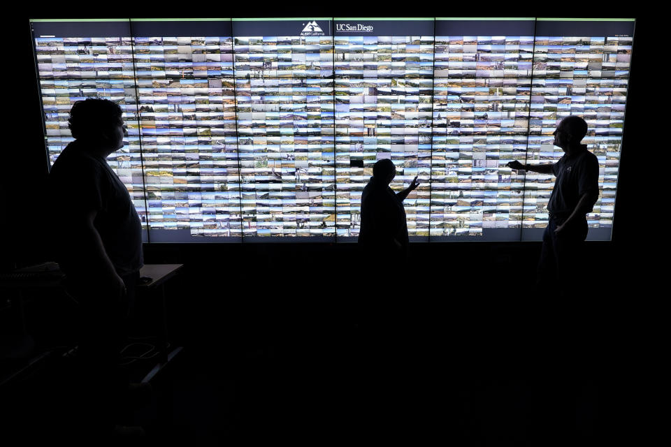 Falco Kuester, right, a researcher at ALERTCalifornia, a program run by the University of California San Diego, looks at live feeds from some of the program's cameras alongside analyst Scott McAvoy, left, and communications manager Caitlin Scully, Monday, Sept. 18, 2023, in San Diego. California's main firefighting agency, Cal Fire, in July started trying out an artificial intelligence system that looks for smoke from more than 1,000 mountaintop cameras feeds. (AP Photo/Gregory Bull)