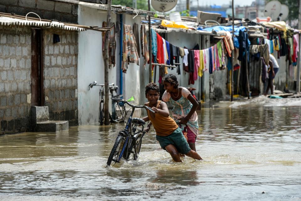 TOPSHOT - Children push a bicycle making their way on a flooded street following heavy rains in Hyderabad on October 15, 2020. (Photo by NOAH SEELAM / AFP) (Photo by NOAH SEELAM/AFP via Getty Images)