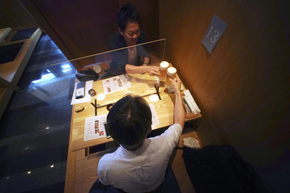 FILE - In this June 4, 2020, file photo, customers drink a toast through plastic protector against new coronavirus infection at Kichiri, an "izakaya" restaurant chain in Tokyo. Japan’s economy is opening cautiously, with social-distancing restrictions amid the coronavirus pandemic. (AP Photo/Eugene Hoshiko, File)