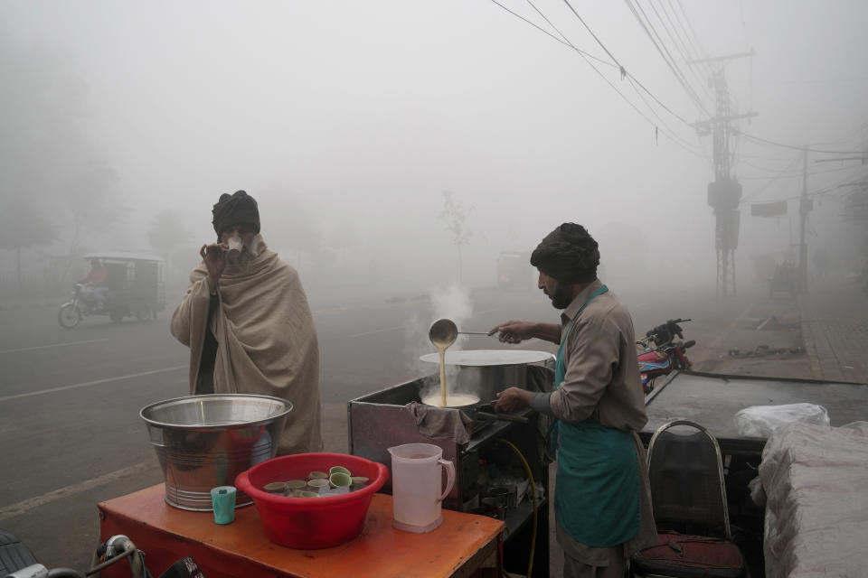 A man drinks tea at a roadside stall as heavy fog reduces visibility in Lahore, Pakistan, Monday, Jan. 2, 2023. (AP Photo/K.M. Chaudary)