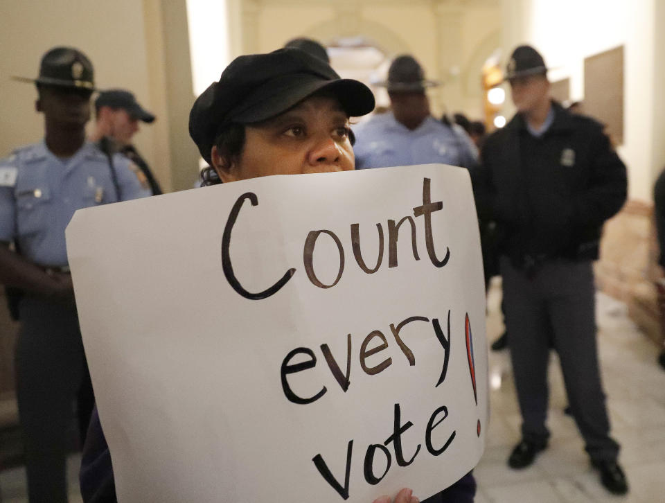 A woman holds a sign as state troopers look on during a protest in the rotunda of the state capitol building Tuesday, Nov. 13, 2018, in Atlanta. Several protesters, including a state senator, have been arrested during a demonstration at the Georgia state Capitol calling for tallying of uncounted ballots from last week's election. (AP Photo/John Amis)