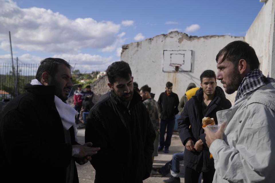 Migrants from Afghanistan gather at an old school used as a temporary shelter on the island of Kythira, southern Greece, Friday, Oct. 7, 2022. Strong winds were hampering rescue efforts at two Greek islands Friday for at least 10 migrants believed to be missing after shipwrecks left more than 20 people dead, officials said. (AP Photo/Thanassis Stavrakis)