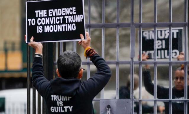 An anti-Trump activist holds a sign in front of the Wall of Silence installation by Donna Ferrato on display at a park across the street from the Manhattan criminal court.