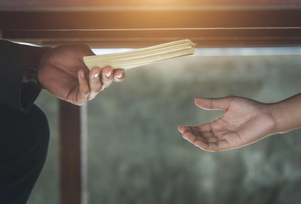 Image showing a man's hand handing over a stack of money under the table to another, to illustrate a story on an ex-SIA manager being charged for taking bribes. 