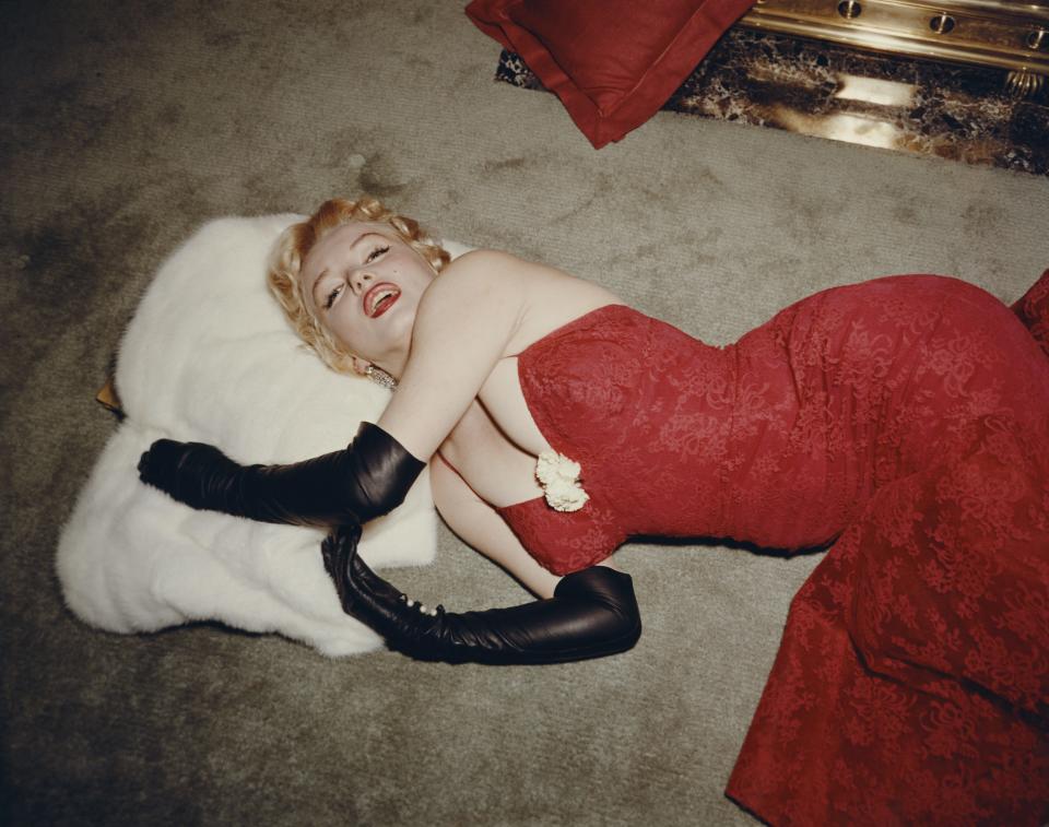 Marilyn Monroe in a red brocade evening gown and long black gloves, using a white fur stole as a pillow.