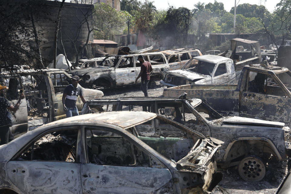 Dos personas buscan piezas útiles entre los autos quemados en un taller mecánico que ardió a causa de la violencia entre bandas armadas en Puerto Príncipe, Haití, el 25 de marzo de 2024. (AP Foto/Odelyn Joseph)