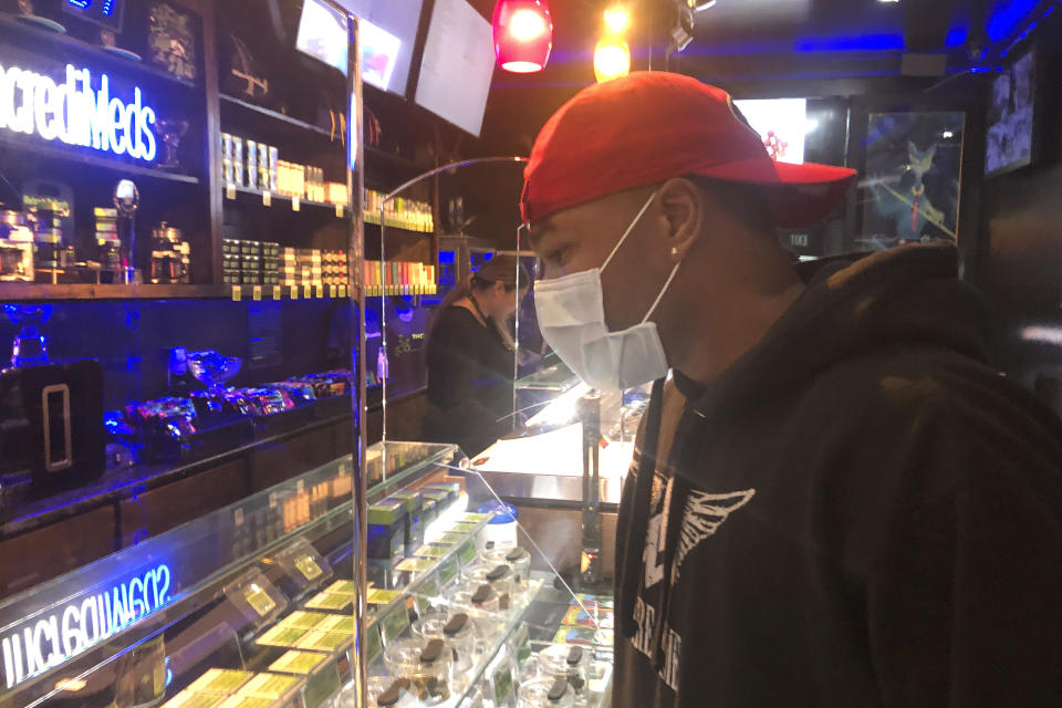 A customer who wished to remain unidentified wears a mask while shopping at The Green Cross cannabis dispensary in San Francisco, Wednesday, March 18, 2020. As about 7 million people in the San Francisco Bay Area are under shelter-in-place orders, only allowed to leave their homes for crucial needs in an attempt to slow virus spread, marijuana stores remain open and are being considered "essential services." (AP Photo/Haven Daley)