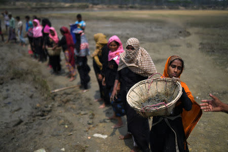 Rohingya refugee women carry baskets of dried out mud from the riverbed to help raise the ground level of the camp in preparation for monsoon season, in Shamlapur refugee camp in Cox's Bazaar, Bangladesh, March 24, 2018. REUTERS/Clodagh Kilcoyne