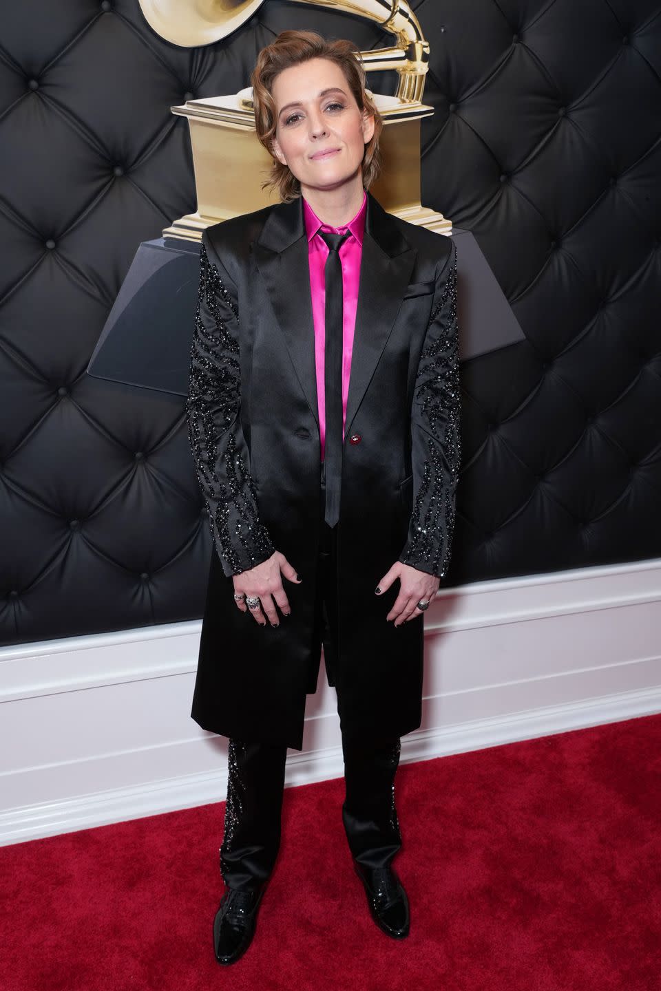<p>Brandi Carlile knows about a good suit, and tonight she opted for a black satin two-piece suit by Versace, worn with a hot pink button-down shirt and an ultra-skinny black tie. The suit hit at her knees with sleeves and side panels adorned with black sequin embroidery. For footwear, she went with oxfords, which frankly more celebrities should consider instead of the standard pump.</p>