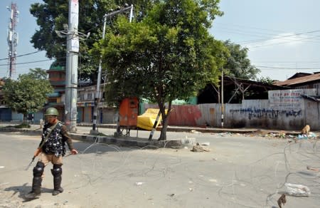 An Indian policeman lays concertina wire across a road during restrictions in Srinagar