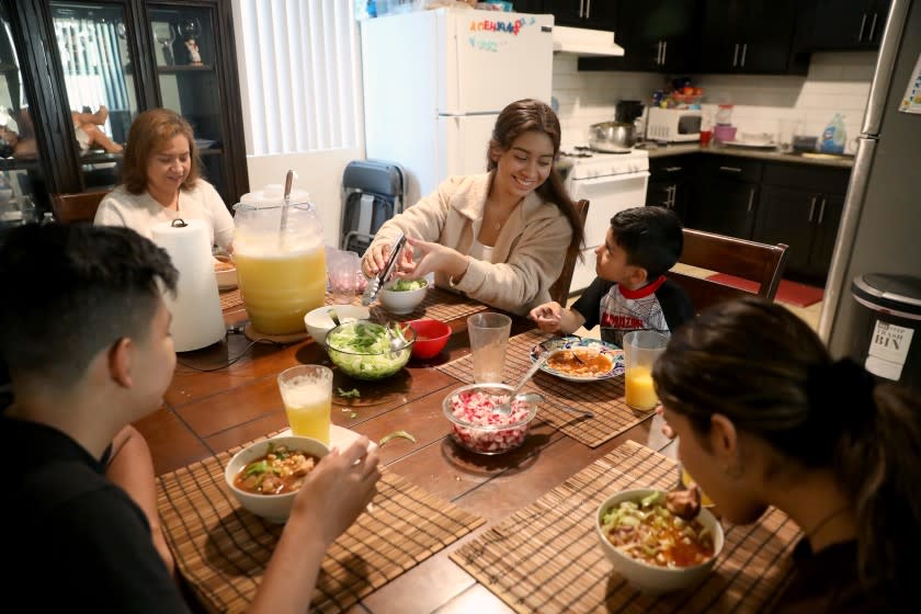 LOS ANGELES, CA - DECEMBER 11: Stephanie Contreras-Reyes, 17, center, a senior at Orthopaedic Hospital Medical Magnet High School, eats homemade pozole with brother Ismael Contreras-Reyes, 13, from left, mother Teresa Reyes, brother Cristian Contreras-Reyes, 5, and sister Ashley Contreras-Reyes, 16, on Friday, Dec. 11, 2020 in Los Angeles, CA. Contreras-Reyes, who does it all - helps her younger siblings with classes, leads her own club, and works with her mom Teresa Reyes at an embroidery factory. An increasing number of high schoolers have started working more hours - or working for the first time - to keep their families afloat. (Gary Coronado / Los Angeles Times)