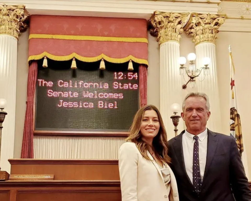 Jessica standing with Robert F. Kennedy Jr. in front of a sign saying "The California state senate welcomes Jessica Biel"