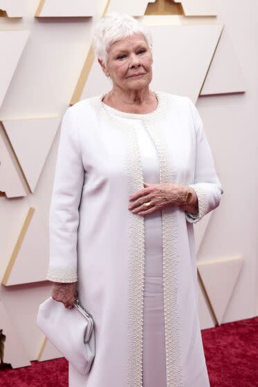 A woman stands on a red carpet dressed in white.