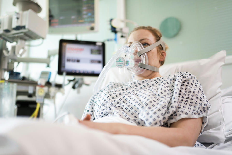 In this Friday, March 27, 2020 photo provided by UCLH a female volunteer demonstrates the use of a CPAP device at UCL Hospital in London. Formula One team Mercedes has helped to develop a breathing aid that could keep coronavirus patients out of intensive care and ease some pressure on Britain’s strained health service. Mercedes worked with engineers at the University College London and clinicians at University College London Hospital in a combined effort involving seven Britain-based teams to adapt and improve a device that bridges the gap between an oxygen mask and the need for full ventilation. (UCLH via AP)