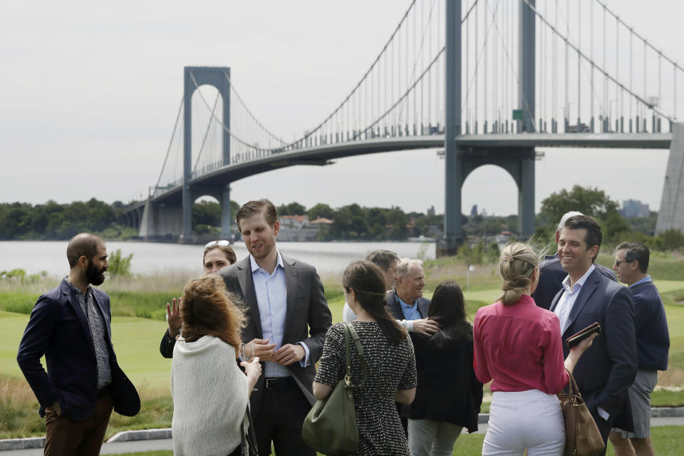 In this June 11, 2018 photo, President Donald Trump's sons, Eric Trump, third from left, and Donald Trump Jr., second from right, talk with guests at the opening of the Trump Golf Links clubhouse in the Bronx borough of New York. Behind them is the Whitestone Bridge. President Donald Trump's company posted annual losses at his golf course in the Bronx for the first time since it opened four years ago as expenses rose, greens fees barely budged and the opening of a clubhouse was delayed. (AP Photo/Mark Lennihan)