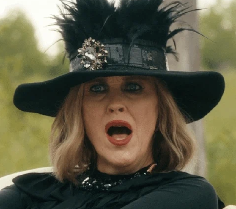 Moira Rose from Schitt's Creek is wearing a dramatic hat with feathers and dark, elegant clothing. She appears to be surprised or shocked. CBC, #SchittsCreek