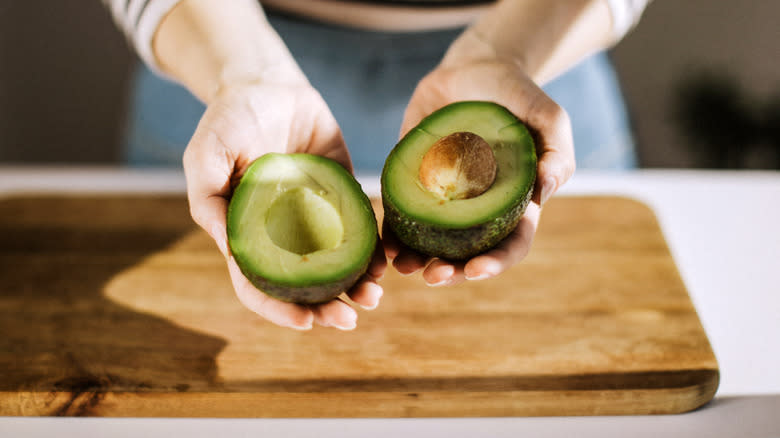 hands holding halved avocado over cutting board