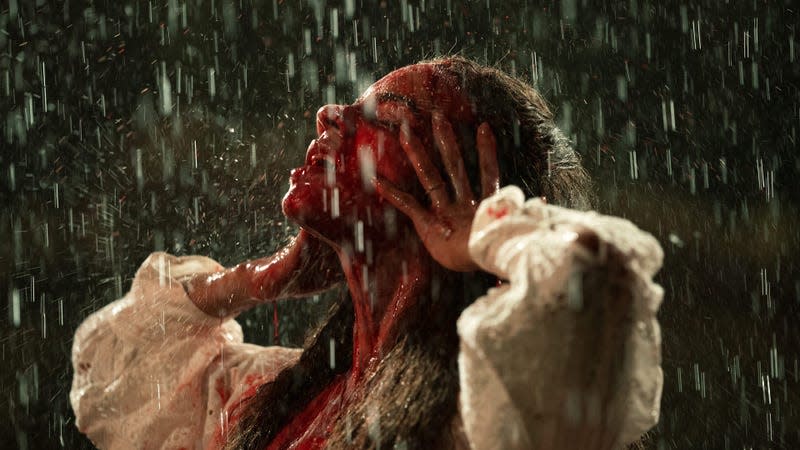 A woman with blood on her face looks up into the rain