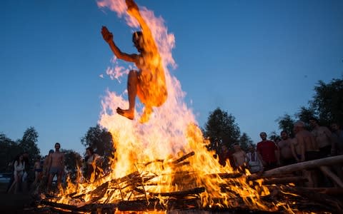 A man jumps over a bonfire during festivities marking Ivan Kupala Day, a pagan summer solstice celebration, in the village of Fadino on the Irtysh River - Credit: Dmitry Feoktistov/TASS