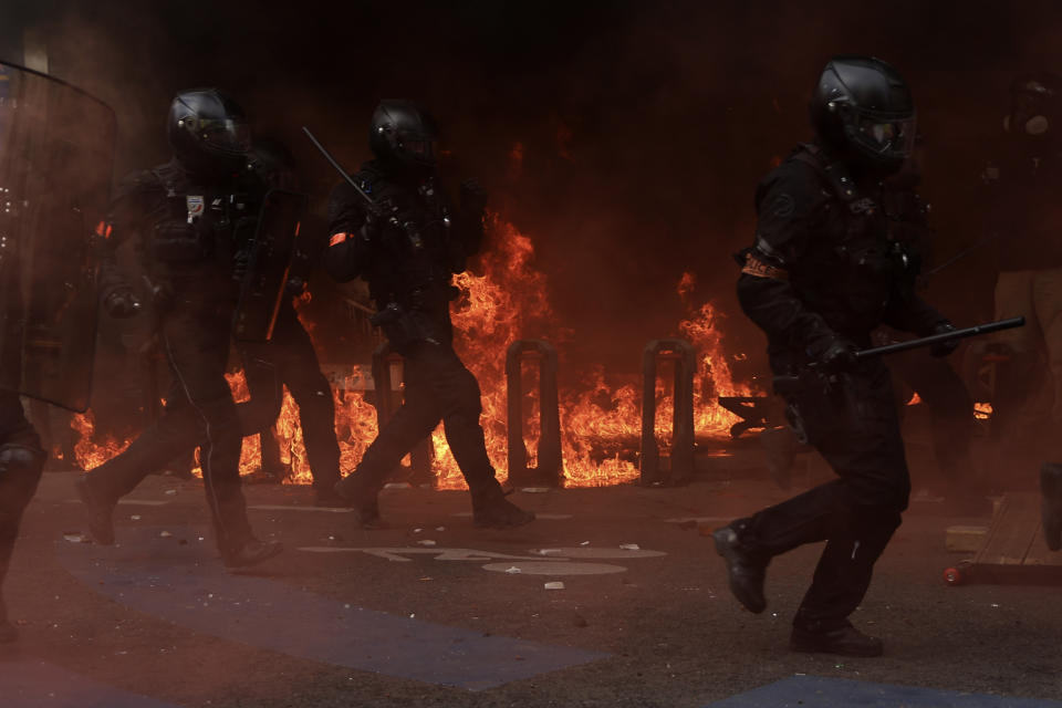 Riot police officers run next to a fire set in front of a building during a demonstration in Paris, Monday, May 1, 2023. Across France, thousands marched in what unions hope are the country's biggest May Day demonstrations in years, mobilized against President Emmanuel Macron's recent move to raise the retirement age from 62 to 64. (AP Photo/Aurelien Morissard)