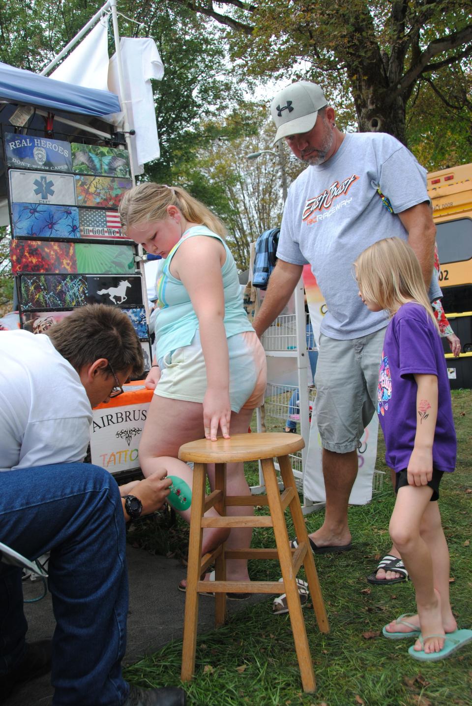 The Airbrush Tattoos artist Ryan Shumaker paints a flower on Miranda McCorkle's leg under the watchful eyes of her dad, Dave, and sister Aubrey, all of Somerset, during last year's annual Confluence PumpkinFest celebration.
(Photo: Staff photo by Madolin Edwards)
