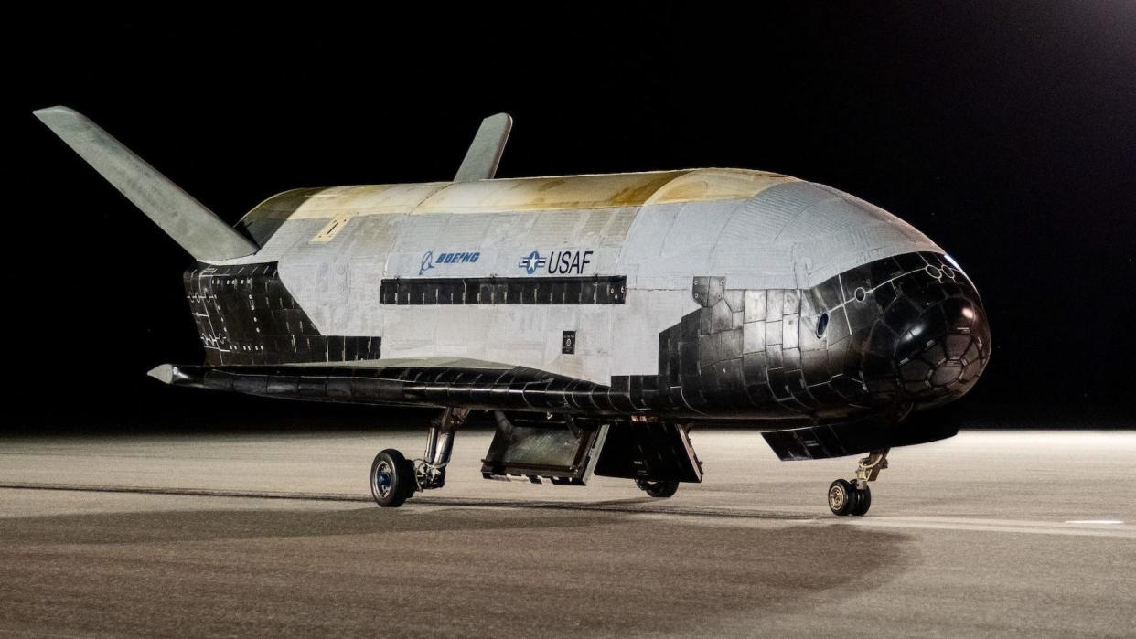 The X-37B Orbital Test Vehicle-6 is shown on a featureless tarmac at night. The spacecraft has no windows
