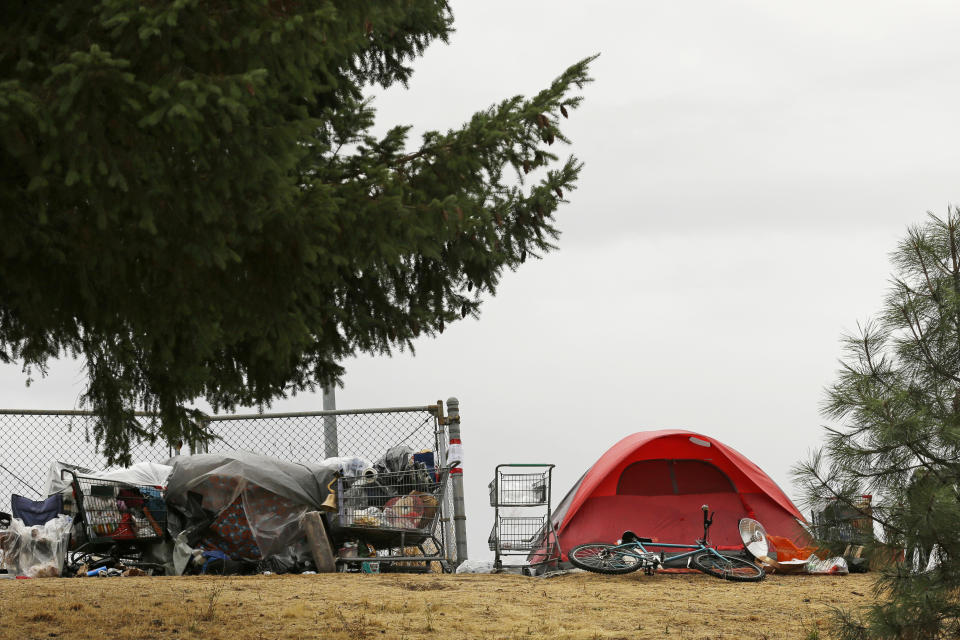 FILE - In this Sept. 19, 2017, file photo, a tent and shopping carts filled with belongings are near a neighborhood in Portland, Ore. Voters in metropolitan Portland will be asked Tuesday, May 19, 2020 to approve taxes on personal income and business profits that would raise $2.5 billion over a decade to fight homelessness even as Oregon grapples with the coronavirus pandemic and its worst recession in decades. (AP Photo/Ted S. Warren, File)