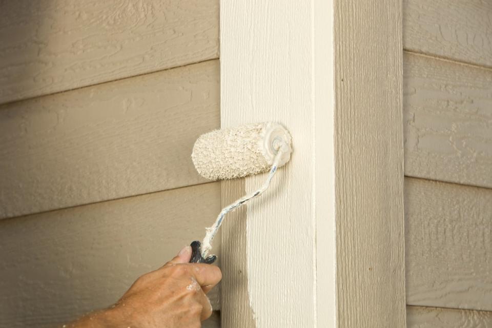 close view of siding on house with paint roller painting white paint on siding