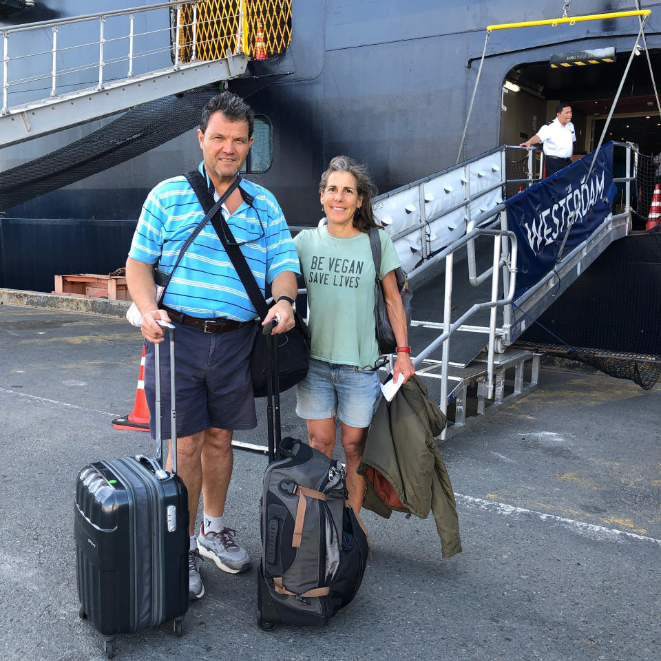 In this Feb. 15, 2020, photo, American couple John and Lydia Miller from Washington state pose for a souvenir photo outside the MS Westerdam while it was docked in Sihanoukville, Cambodia. Having finally reached a friendly port willing to accept them and stepped ashore after weeks of uncertainty at sea, hundreds of cruise ship passengers eyed warily over fears of a new virus are now simply trying to find a way home. (Lydia Miller via AP)