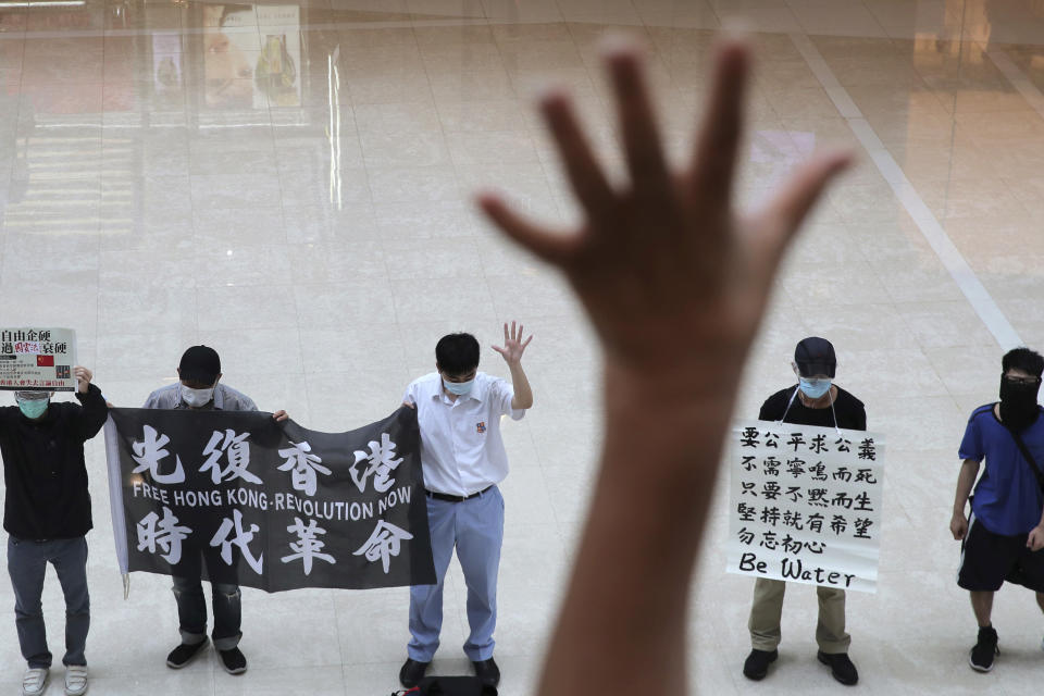 Protesters gesture with five fingers, signifying the "Five demands - not one less" in a shopping mall during a protest against China's national security legislation for the city, in Hong Kong, Friday, May 29, 2020. The British government says t it will grant hundreds of thousands of Hong Kong residents greater visa rights if China doesn't scrap a planned new security law for the semi-autonomous territory. U.K. Foreign Secretary Dominic Raab said about 300,000 people in Hong Kong who hold British National (Overseas) passports will be able to stay in Britain for 12 months rather than the current six. (AP Photo/Kin Cheung)